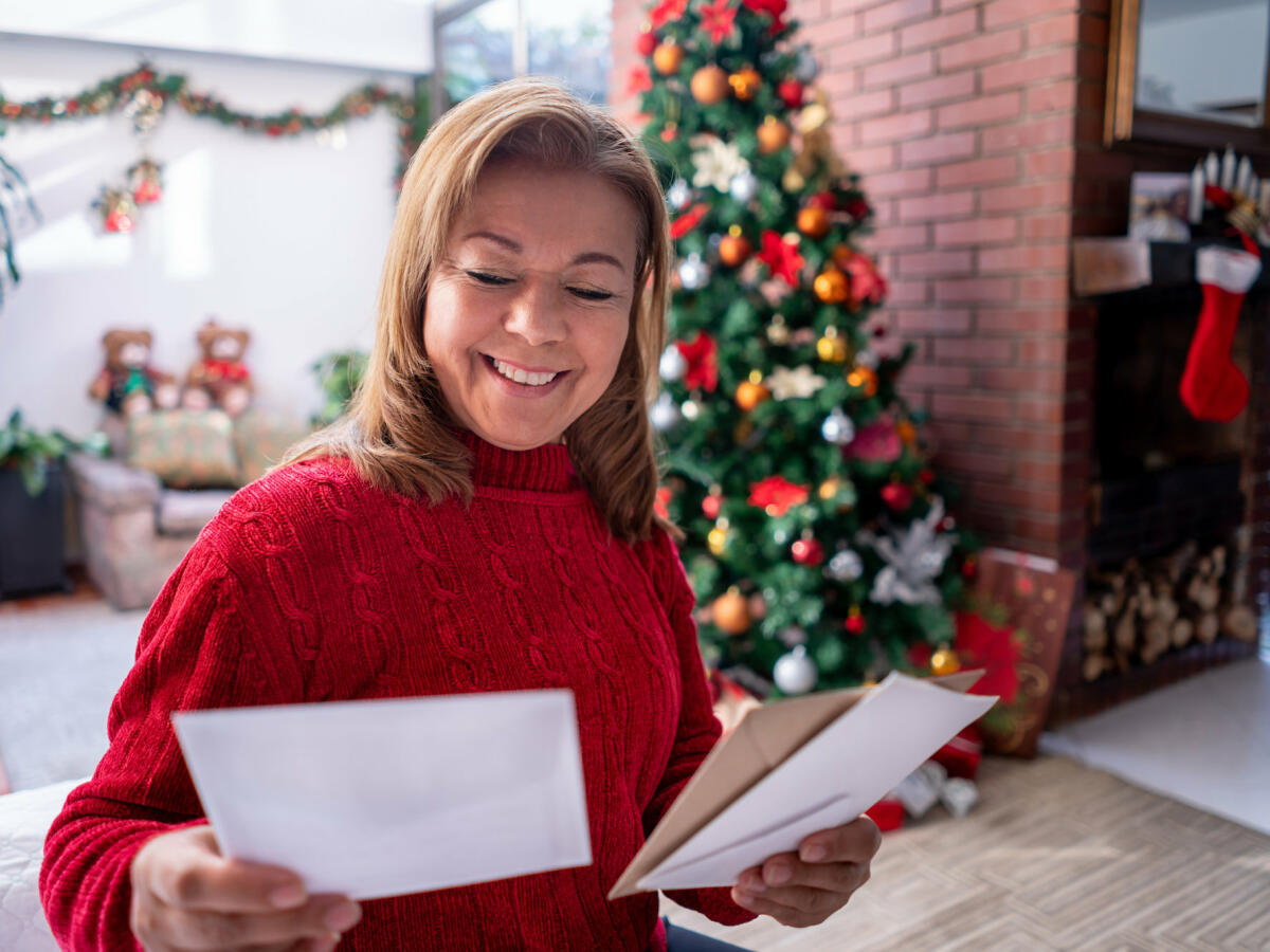 Schöne reife Frau, die alle Weihnachtskarten betrachtet, die sie erhalten hat, während sie sehr glücklich lächelt © Hispanolistic / Getty Images