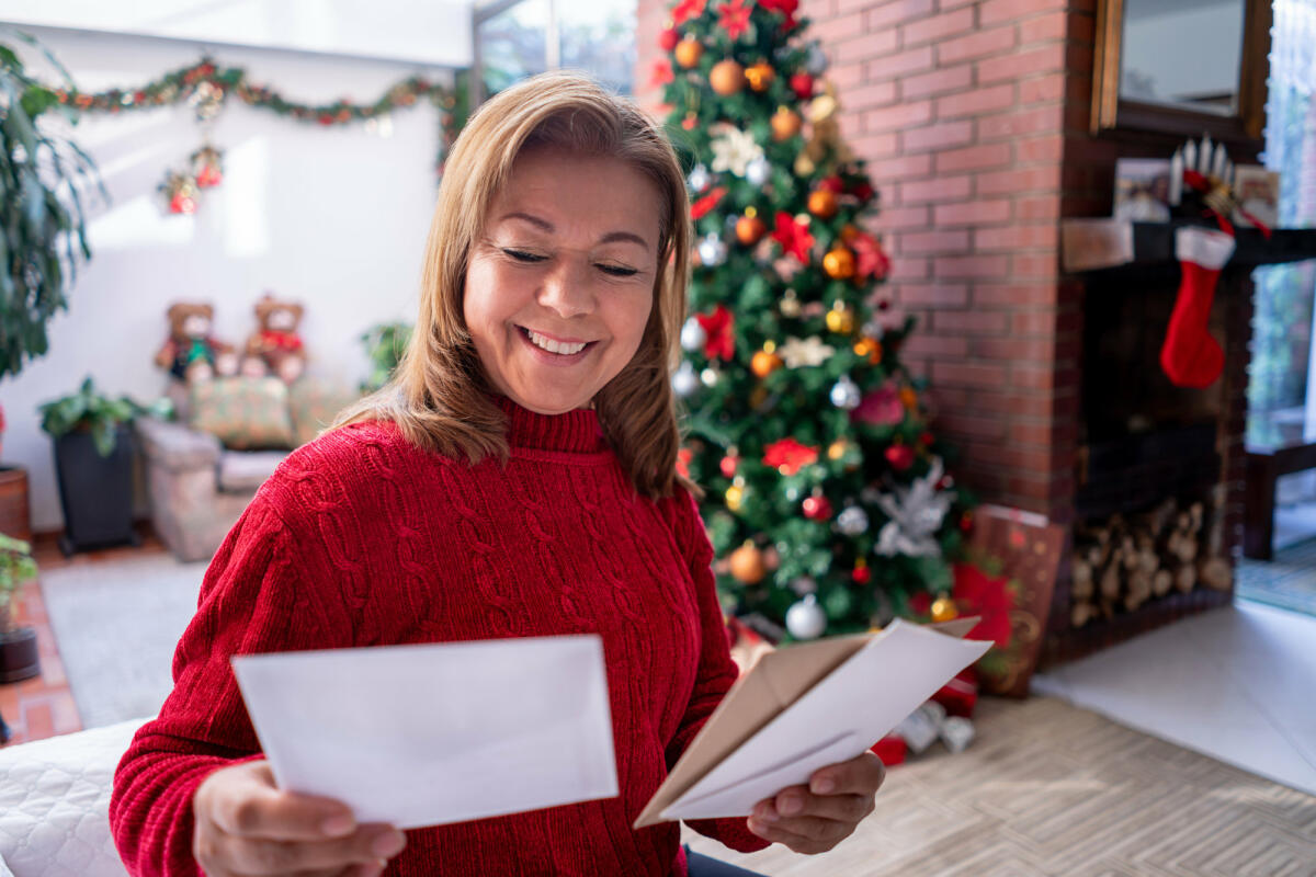 Schöne reife Frau, die alle Weihnachtskarten betrachtet, die sie erhalten hat, während sie sehr glücklich lächelt © Hispanolistic / Getty Images