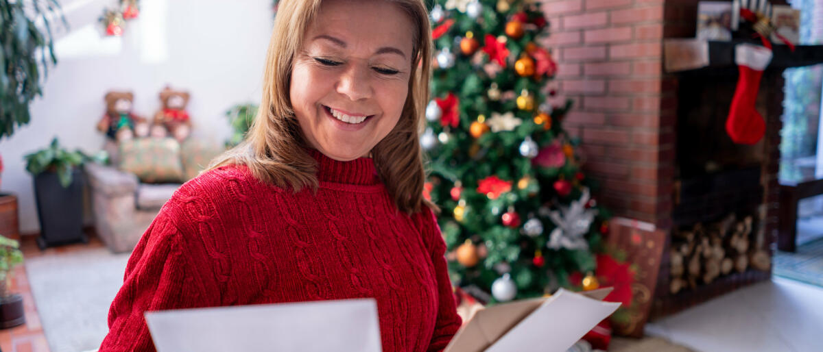 Schöne reife Frau, die alle Weihnachtskarten betrachtet, die sie erhalten hat, während sie sehr glücklich lächelt © Hispanolistic / Getty Images