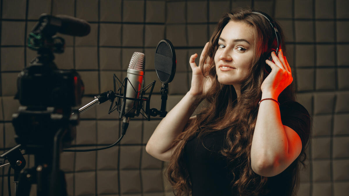 Eine junge Frau steht im Tonstudio mit Kopfhörern und nimmt ihre Stimme auf © Dmytro Sheremeta / Getty Images