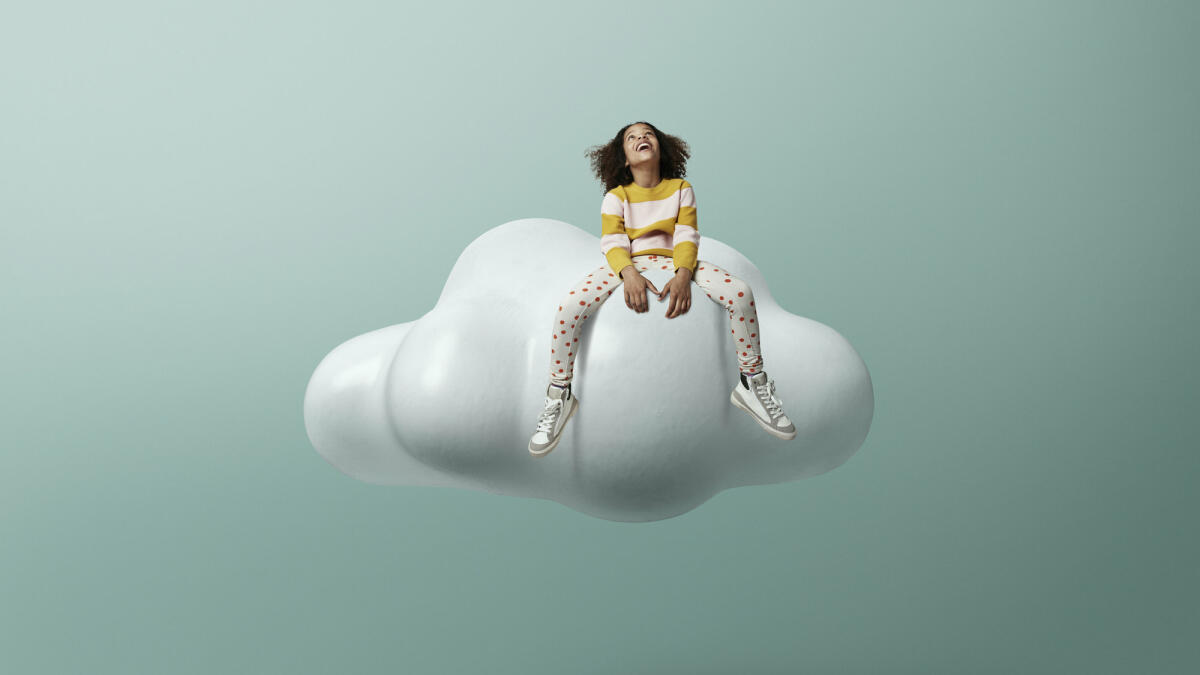 Lachendes Mädchen, das auf einer Wolke sitzend nach oben schaut, vor grünem Hintergrund © Klaus Vedfelt / Getty Images
