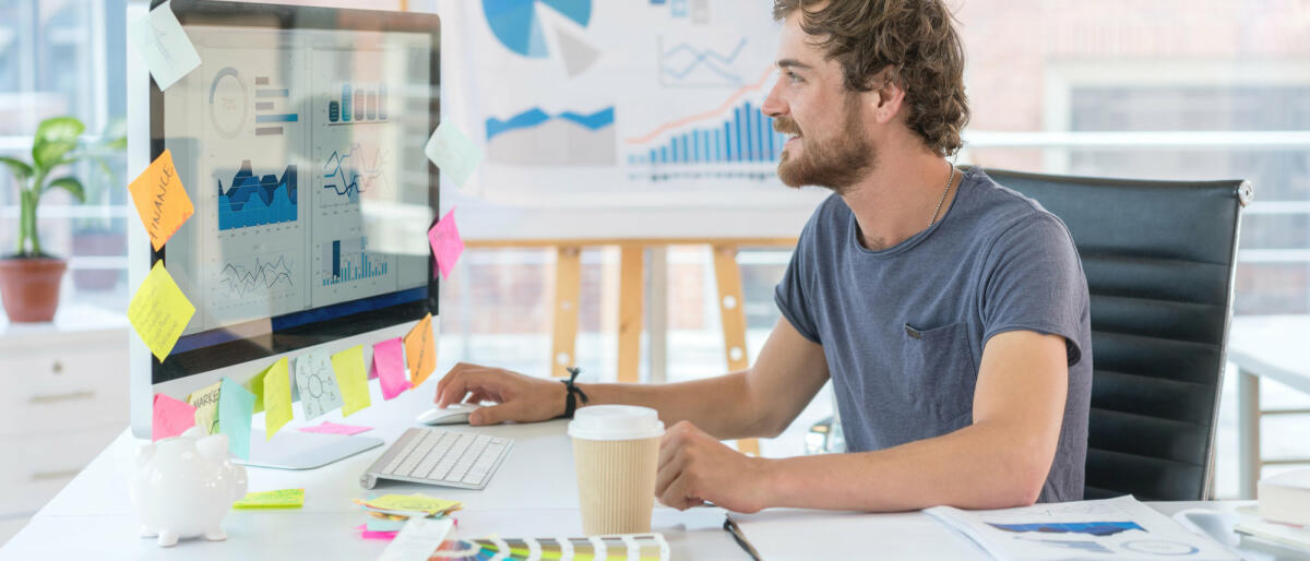 Ein junger Grafikdesigner sitzt vor einem iMac voller Notizzettel © anders / Getty Images