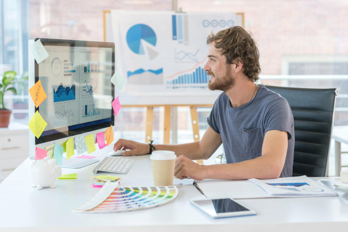 Ein junger Grafikdesigner sitzt vor einem iMac voller Notizzettel © anders / Getty Images