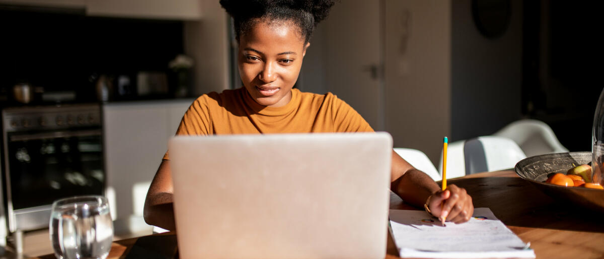 Eine lächelnde Frau sitzt vor ihrem Laptop und schreibt © MStudioImages / Getty Images
