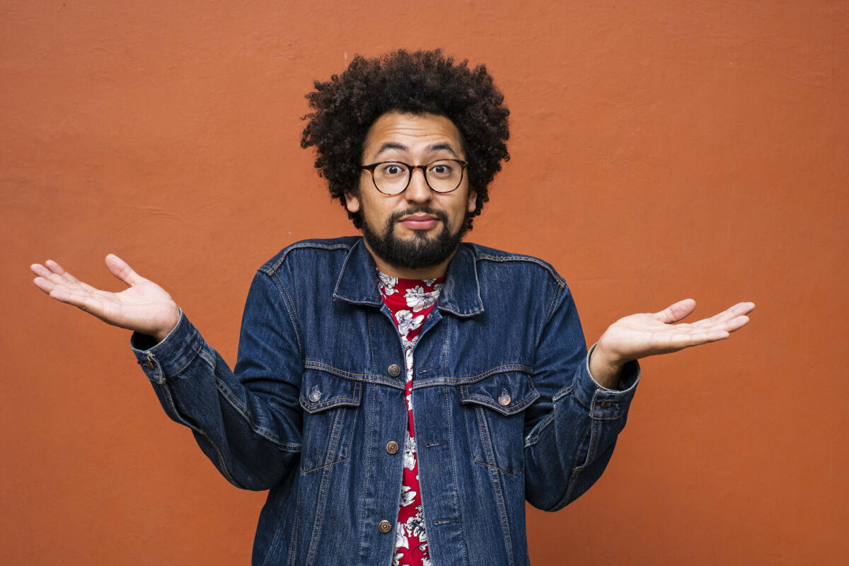 Nicht-binäre Latino-Person mit Brille und Afrofrisur zuckt mit den Schultern und schaut in die Kamera © Sergio Mendoza Hochmann / Getty Images
