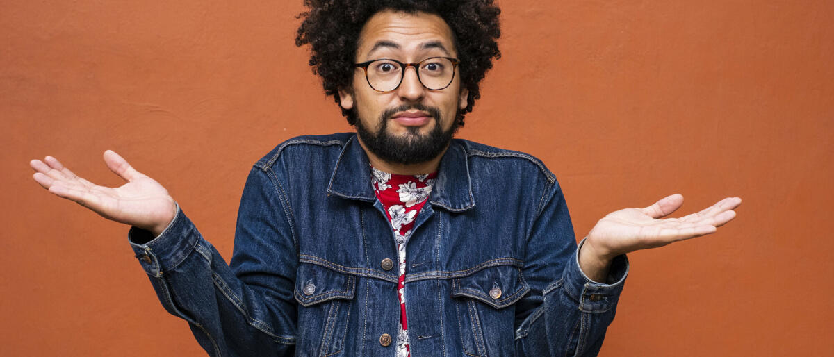 Nicht-binäre Latino-Person mit Brille und Afrofrisur zuckt mit den Schultern und schaut in die Kamera © Sergio Mendoza Hochmann / Getty Images