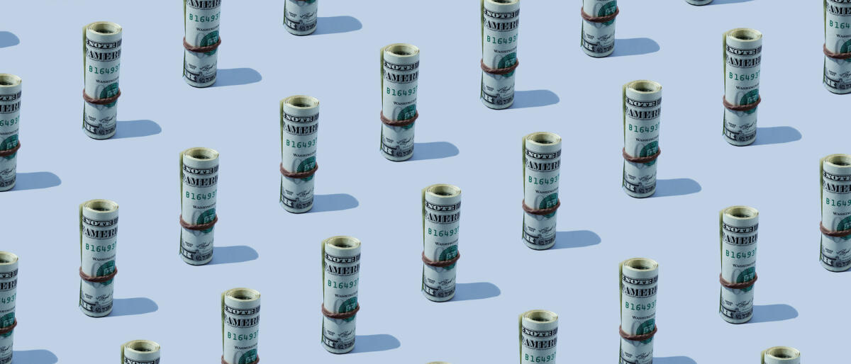 Wiederholte Rollen von amerikanischen Dollar-Banknoten auf dem blauen Hintergrund © Yulia Reznikov / Getty Images