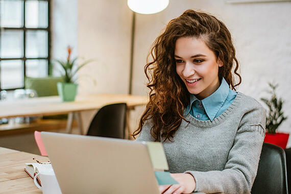 Junge Frau sitzt lächelnd vor Laptop © nortonrsx / Getty Images