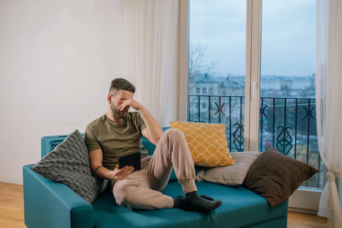 Mann sitzt mit einem Tablet auf dem Sofa und greift sich an den Kopf © Alena Darmel / Pexels