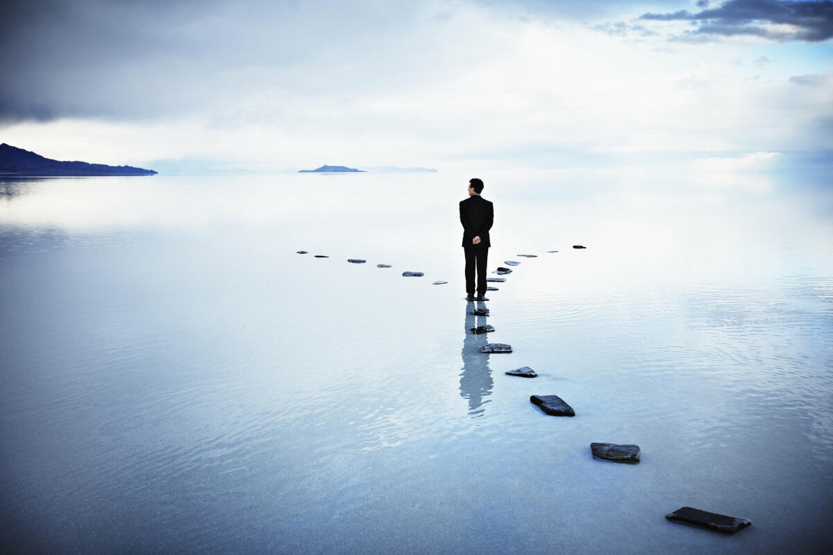 Business-Mann steht auf Steinen im See an Scheideweg © Thomas Barwick / Getty Images