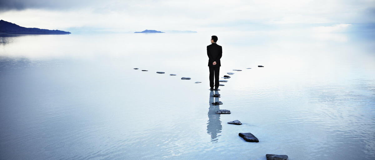 Business-Mann steht auf Steinen im See an Scheideweg © Thomas Barwick / Getty Images