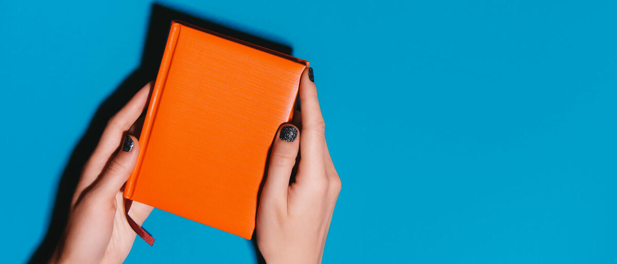Frau Hände halten orange Tagebuch auf hellen Schreibtisch © Olena Ruban / Getty Images