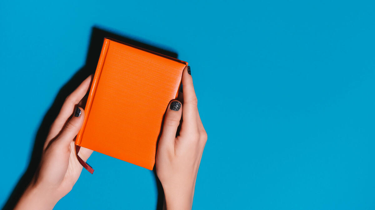 Frau Hände halten orange Tagebuch auf hellen Schreibtisch © Olena Ruban / Getty Images
