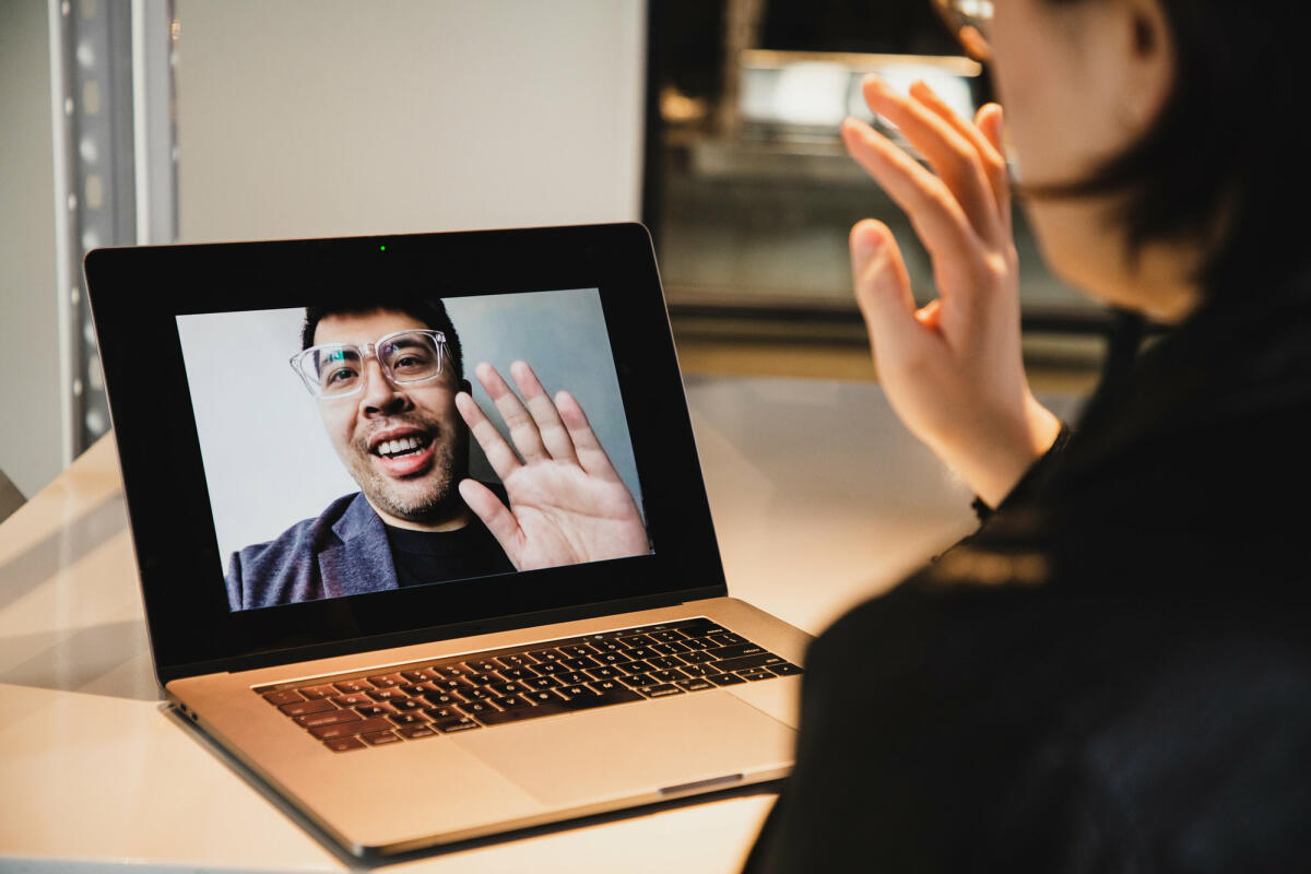 Frau sitzt vor Laptop und winkt Mann in Videokonferenz © Kilito Chan / Getty Images