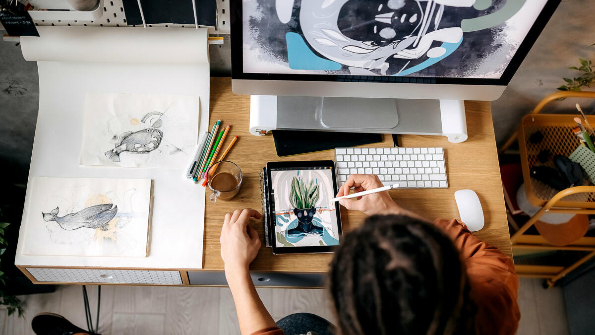 Eine Illustratorin sitzt am Schreibtisch und zeichnet auf ihrem Tablet © Pesic / Getty Images