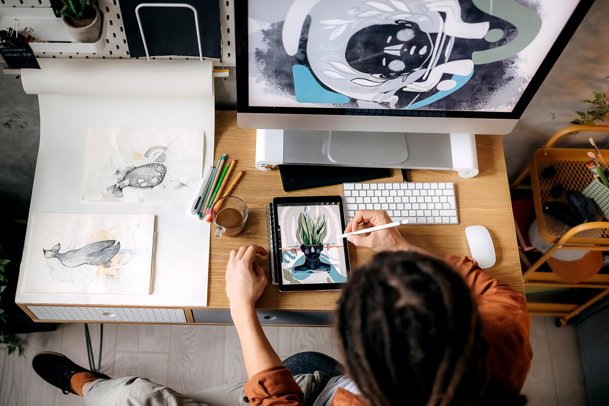 Eine Illustratorin sitzt am Schreibtisch und zeichnet auf ihrem Tablet © Pesic / Getty Images