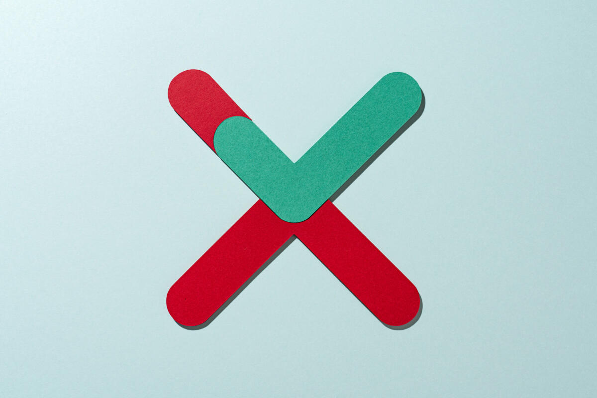 Papierhandwerk Grün gefärbtes Häkchen eingebettet in rot gefärbtes Kreuzzeichen auf grünem Hintergrund direkt über der Ansicht © MirageC / Getty Images