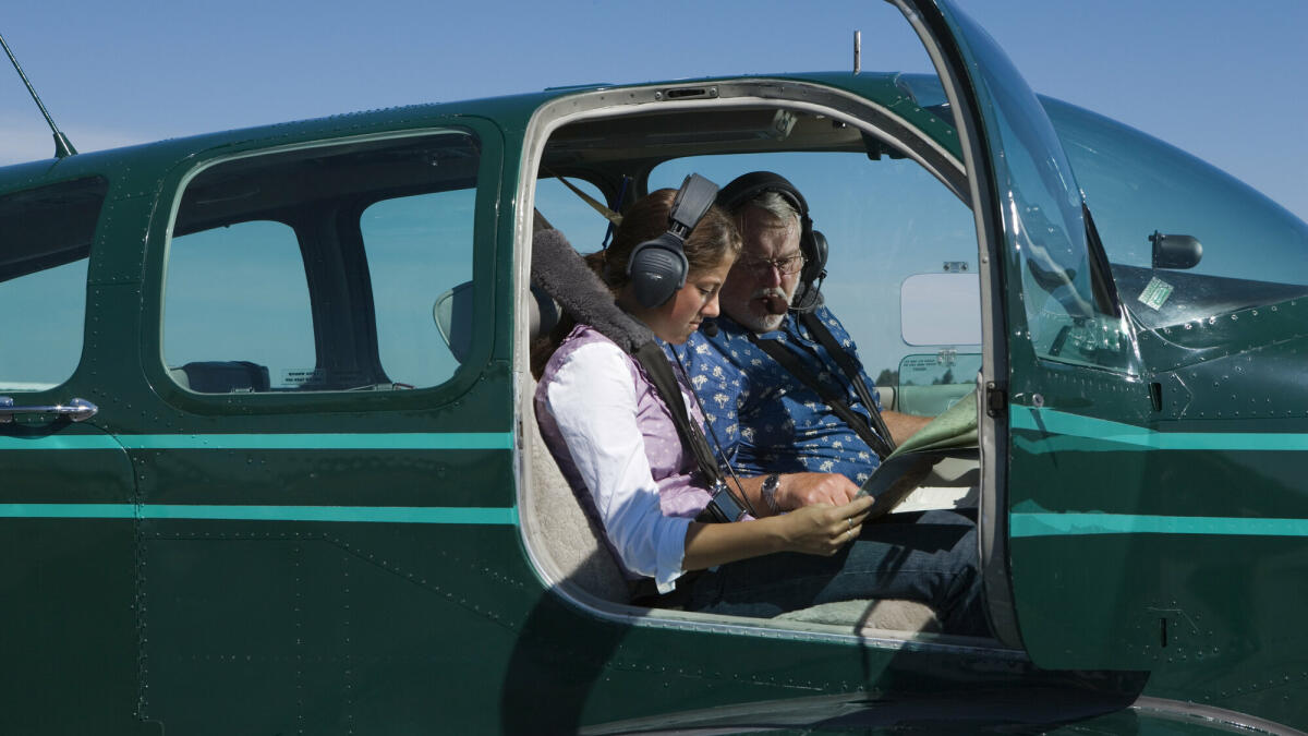 Teenager-Mädchen und Fluglehrer mit Blick auf die Karte im Flugzeug © Karen Moskowitz / Getty Images