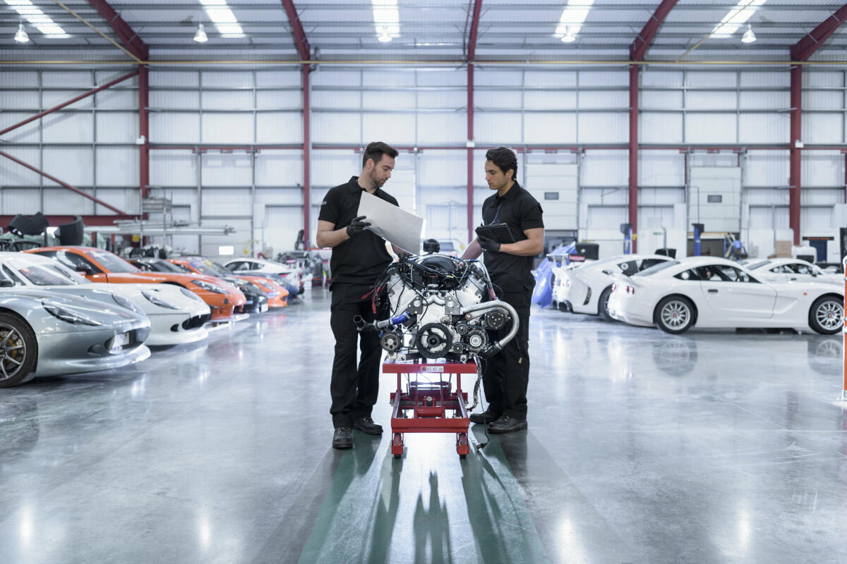 Zwei junge Automobilingenieure stehen vor einem Automotor und beraten sich. © Monty Rakusen / Getty Images