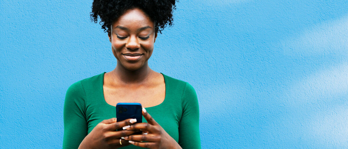 Frau benutzt Smartphone neben blauer Wand © Tim Robberts / Getty Images