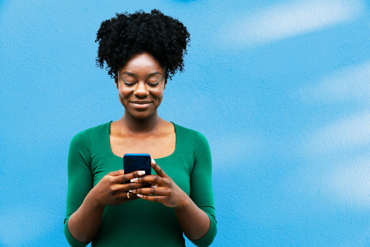 Frau benutzt Smartphone neben blauer Wand © Tim Robberts / Getty Images