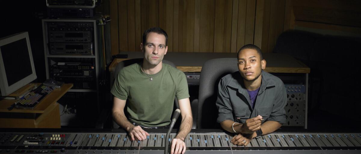 Zwei junge Musikproduzenten sitzen zusammen in einem Tonstudio am Mischpult © Image Source / Getty Images