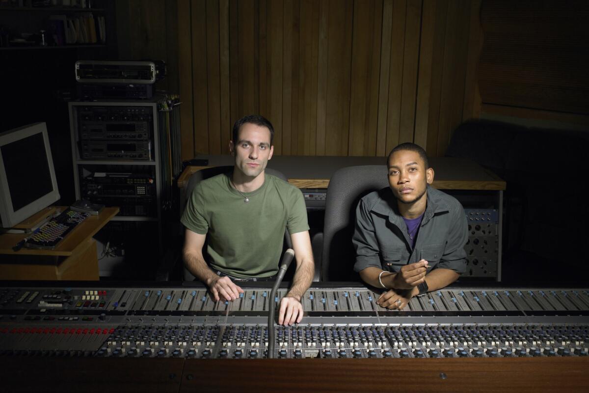 Zwei junge Musikproduzenten sitzen zusammen in einem Tonstudio am Mischpult © Image Source / Getty Images