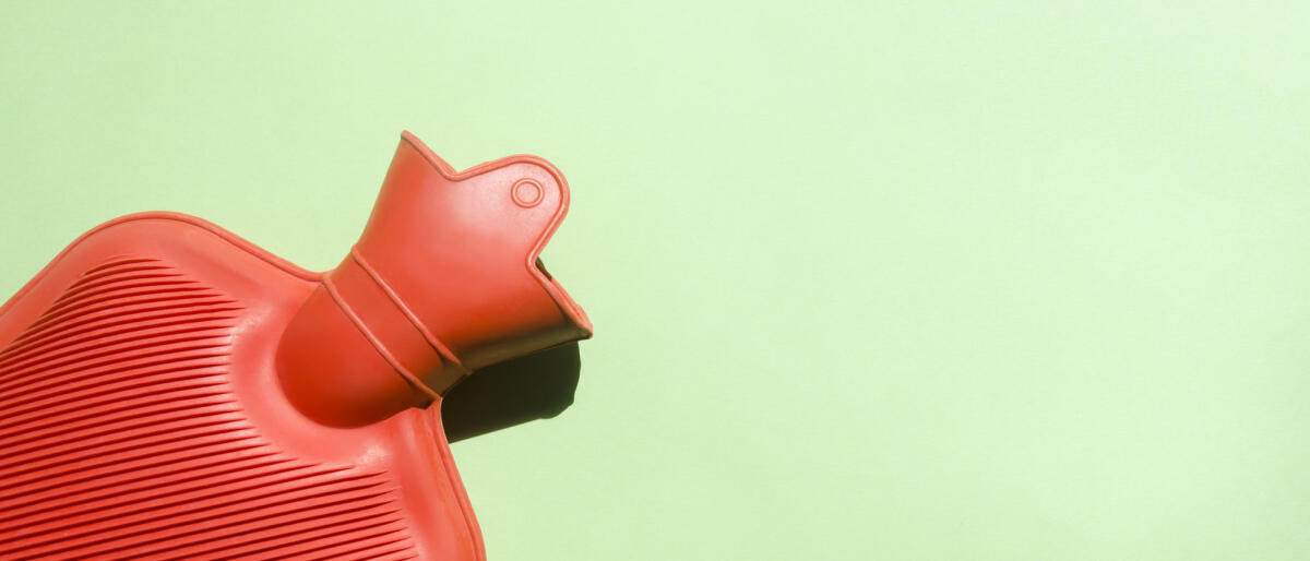 Rote Wärmflasche vor grünem Hintergrund © Elizabeth Fernandez / Getty Images