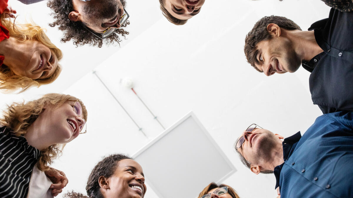 Lächelnde Kollegen, die zusammen im Kreis stehen © Luis Alvarez / Getty Images