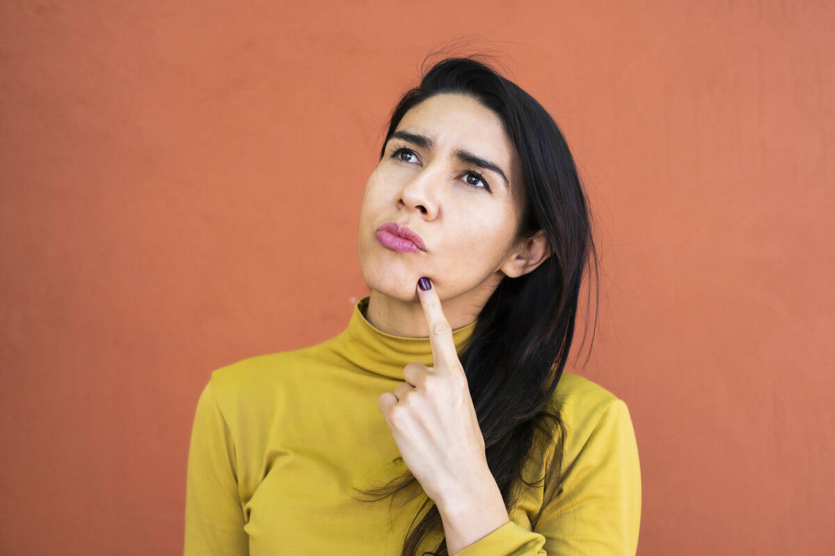 Latino-Frau in Gedanken versunken, nachdenklich und aufblickend, Finger am Kinn © Sergio Mendoza Hochmann / Getty Images